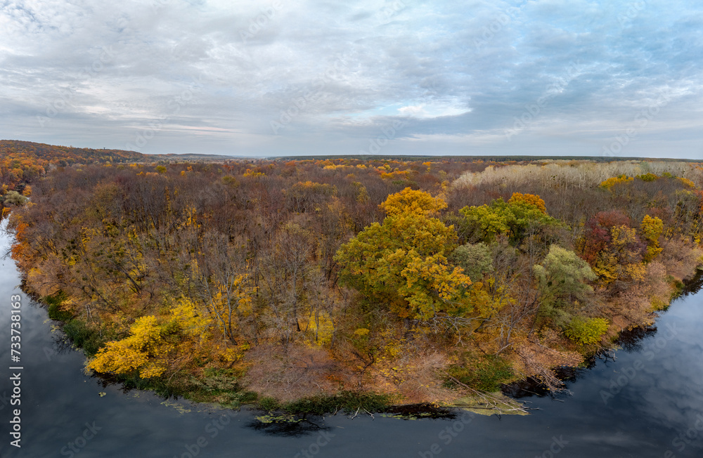 Aerial panorama autumn river with blue mirror water, yellow forest landscape and cloudy sky. Wild riverside nature in Ukraine