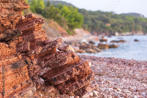 Wild beach Crvena Glavica in Montenegro. Red rocks coast and water waves photo