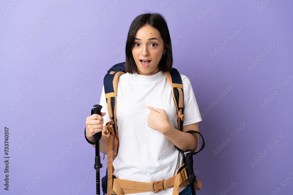 Young caucasian woman with backpack and trekking poles isolated on blue background with surprise facial expression