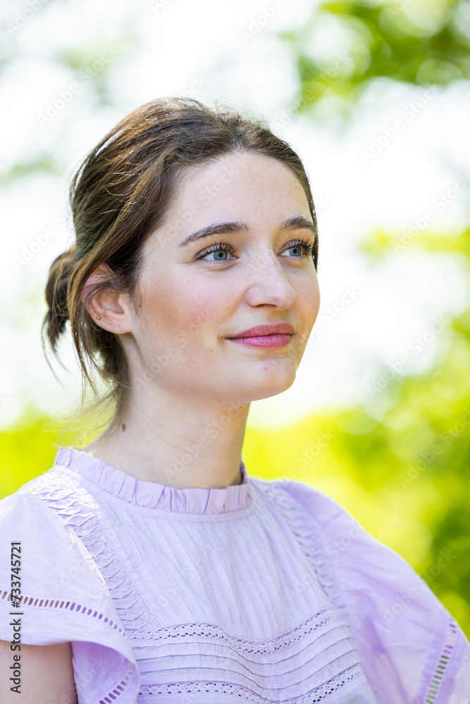 The photograph captures a young woman looking off into the distance with a hopeful and thoughtful expression. The outdoor setting with soft, natural light accentuates her delicate features and the The photograph captures a young woman looking off into the distance with a hopeful and thoughtful expression. The outdoor setting with soft, natural light accentuates her delicate features and the