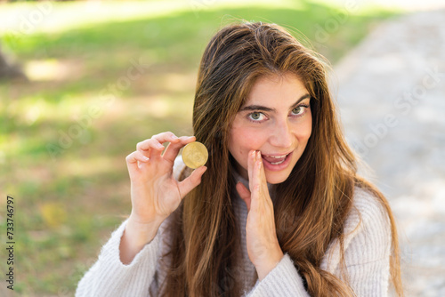 Young pretty caucasian woman holding a Bitcoin at outdoors whispering something