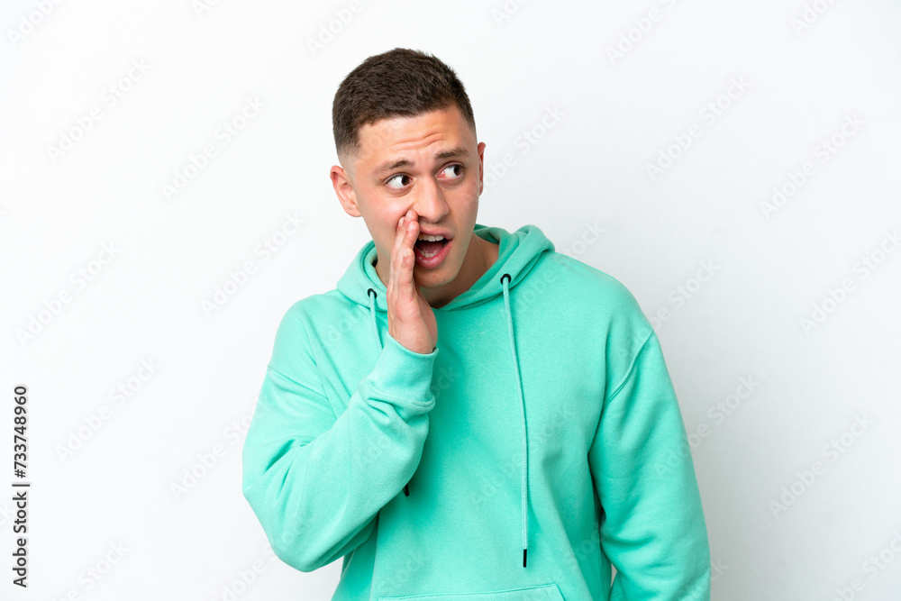 Young brazilian man isolated on white background whispering something with surprise gesture while looking to the side