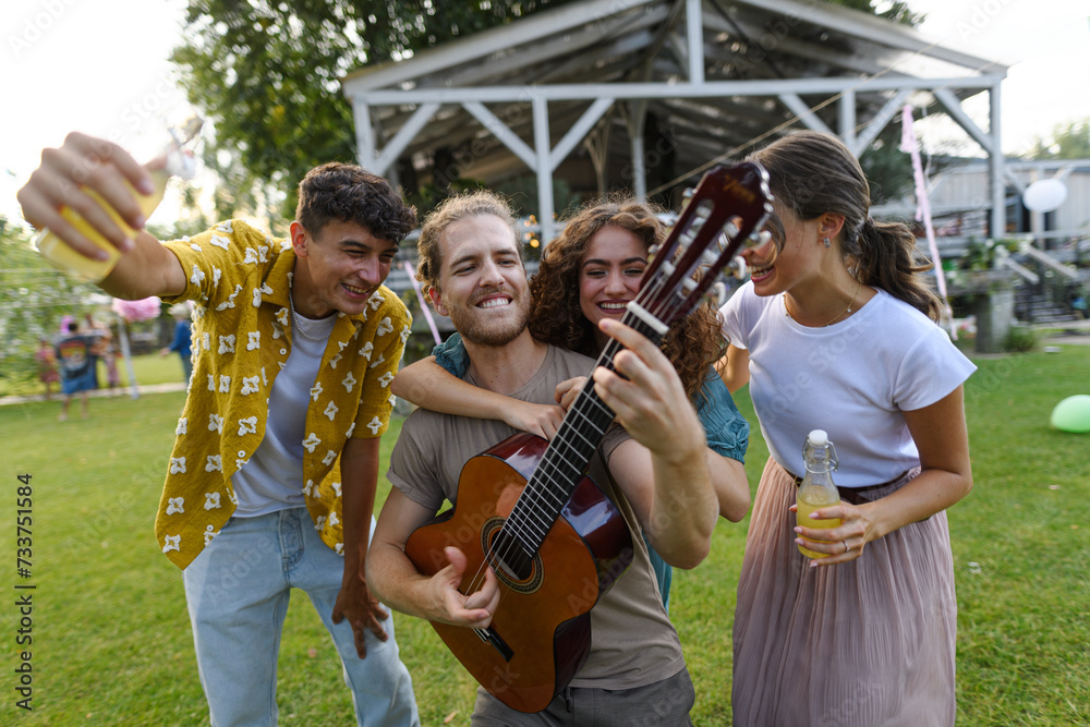Handsome man playing at guitar for dancing friends at party. Friends and family dancing and having fun at summer grill garden party. Handsome man playing at guitar for dancing friends at party. Friends and family dancing and having fun at summer grill garden party.