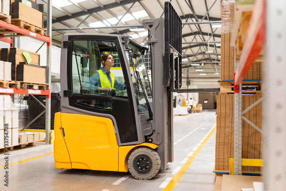 Female warehouse worker driving forklift. Warehouse worker preparing products for shipmennt, delivery, checking stock in warehouse.