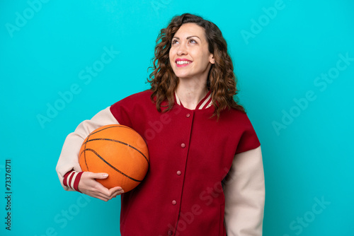 Young caucasian basketball player woman isolated on blue background thinking an idea while looking up