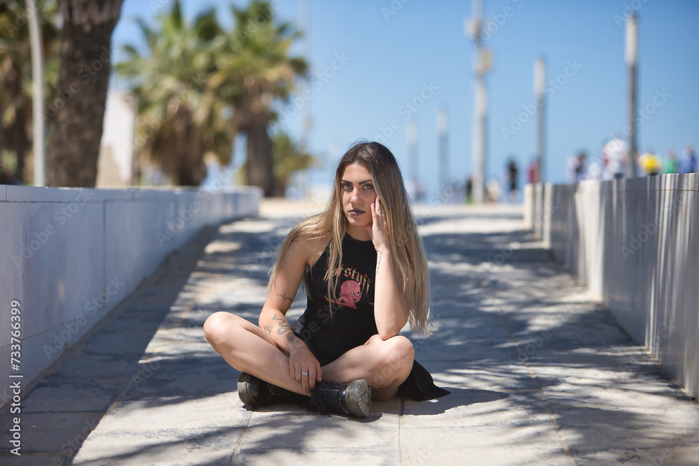 Young, beautiful blonde woman, green eyes, with black top and skirt, tattoos, sitting on the floor, looking at the camera, rebellious and independent. Concept looks, rebelliousness, insubordination. Young, beautiful blonde woman, green eyes, with black top and skirt, tattoos, sitting on the floor, looking at the camera, rebellious and independent. Concept looks, rebelliousness, insubordination.
