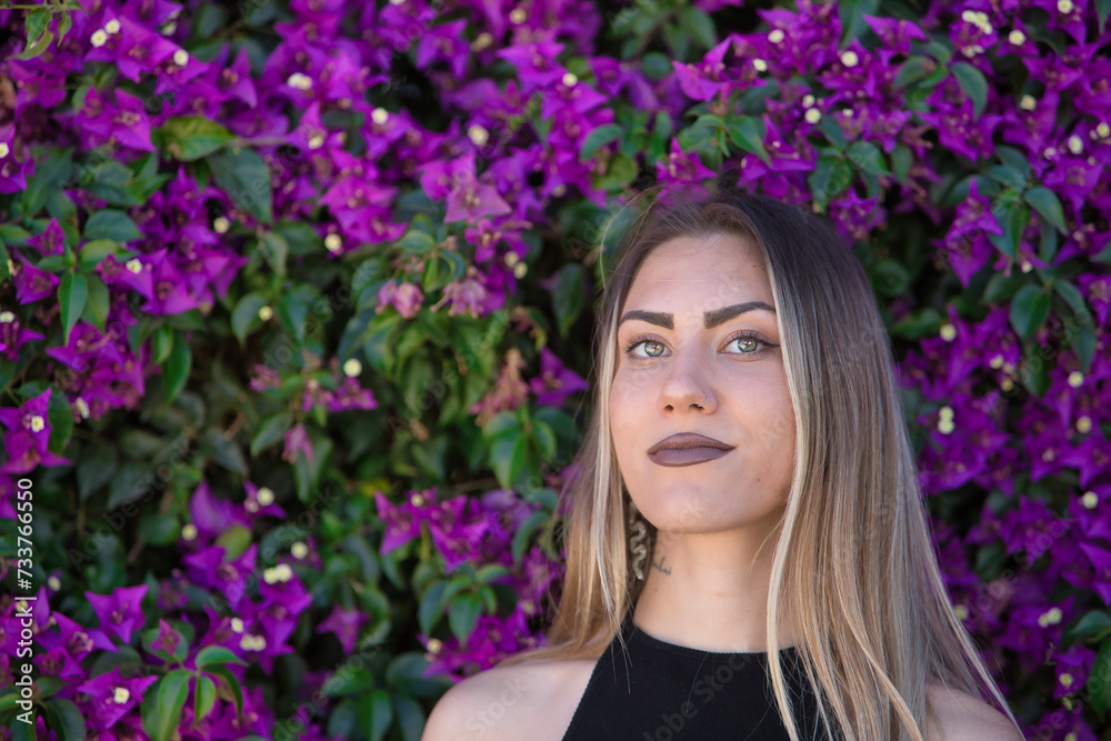 Portrait of a young woman, beautiful, blonde, green eyes, looking at the camera with tender and relaxed attitude with a background of purple bougainvillea. Conceptual looks, eyes, purity, youth. Portrait of a young woman, beautiful, blonde, green eyes, looking at the camera with tender and relaxed attitude with a background of purple bougainvillea. Conceptual looks, eyes, purity, youth.