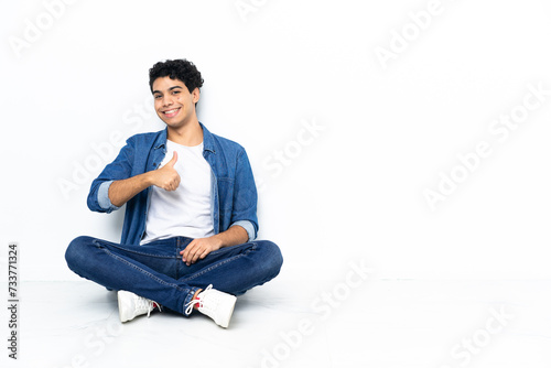 Venezuelan man sitting on the floor giving a thumbs up gesture © luismolinero