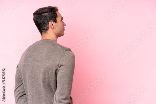 Young caucasian man isolated on pink background in back position and looking back