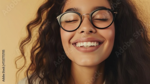 Smiling woman with closed eyes wearing glasses and wavy hair against a soft-focus background.