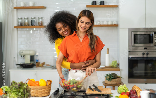 Diversity young happy love LGBT  LGBTQ caucasian and african family lesbian couple woman cook vegan food healthy eat with fresh vegetable salad in kitchen at home  pride  rainbow.Lgbt lesbian couple