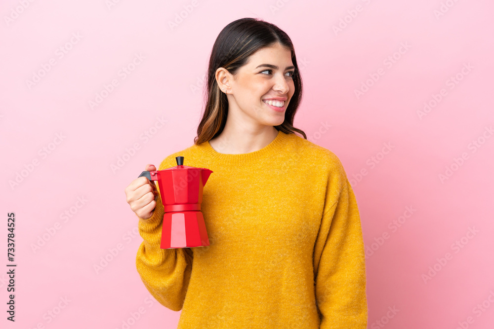 Young Italian woman holding a coffee maker isolated on pink background looking side Young Italian woman holding a coffee maker isolated on pink background looking side