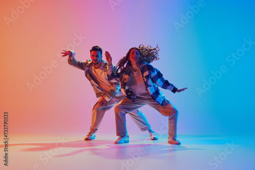 portrait of attractive and fashion dressed pair of dancers performing harmony in motion against gradient studio background. Concept of movement, energy, dance battles. Dynamic gel portrait