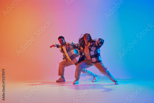 Man and woman, dancing synchronously in motion against gradient studio background. Harmony moves. Concept of fashion and style, movement, energy, dance battles. Dynamic gel portrait