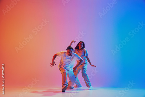 Fototapeta Naklejka Na Ścianę i Meble -  Dynamic lifestyle. Dancers performing hip hop, freestyle in neon lights against gradient studio background. Concept of youth culture, style, movement, energy, dance battles, hobby. Gel portrait