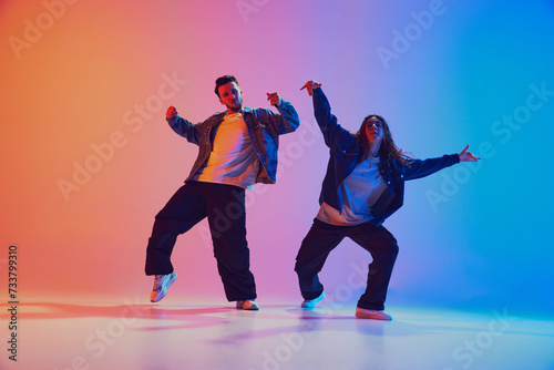 Fototapeta Naklejka Na Ścianę i Meble -  Male and female dancer in sync dressed casual urban wear against gradient background in neon light, filter. Concept of youth culture, music, lifestyle, style and fashion, action. Gel portrait.