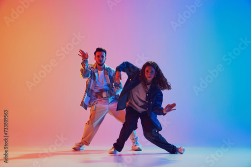 Fototapeta Naklejka Na Ścianę i Meble -  Dynamic lifestyle. Man and woman, hip-hop dance moves sync in motion against gradient studio background in neon light. Concept of youth culture, music, style and fashion, action. Gel portrait.