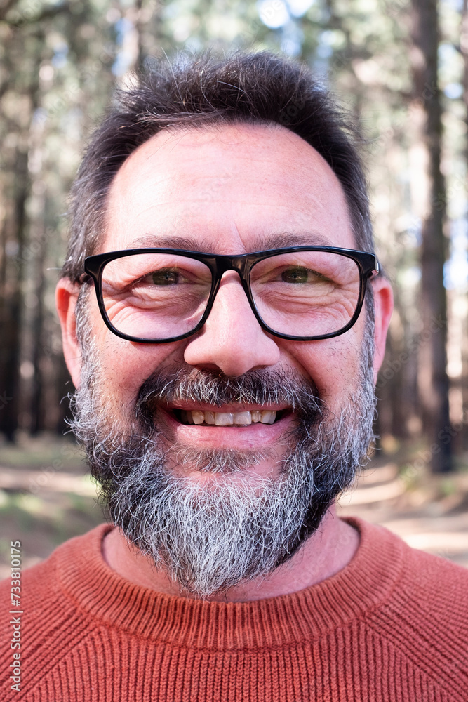 Fototapeta premium Cheerful adult happy man taking selfie picture in the woods enjoying outdoors leisure activity in national forestal park alone. Adventure and lifestyle people. High trees in background. Sustainability