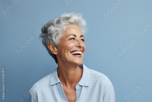 Portrait of happy senior woman with grey hair smiling against blue background © Iigo
