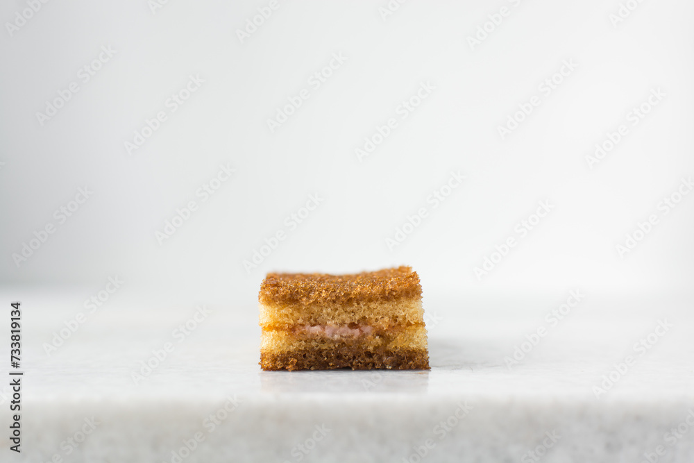 A slice of vanilla cake with jam filling, thin layers of vanilla and chocolate cake with jam filling on a white background A slice of vanilla cake with jam filling, thin layers of vanilla and chocolate cake with jam filling on a white background
