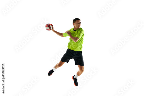 Competitive young guy in uniform, handball player in a jump, throwing ball during game against white studio background. Concept of professional sport, tournament, competition