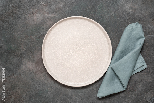 Empty beige plate mockup with blue linen napkin, dark grunge background. Top view, flat lay. Minimal table setting.
