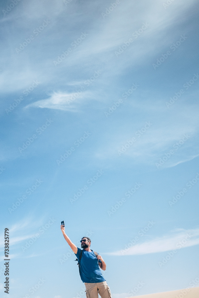 Standing man in outdoor leisure activity check phone internet signal to communicate - concept of internet phone device and communication time in the world - blue sky bckground