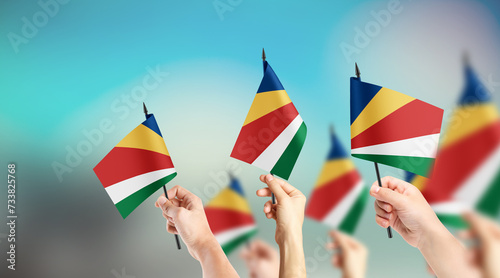 A group of people are holding small flags of Seychelles in their hands.