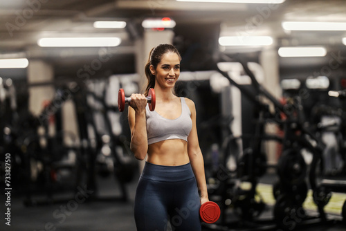A fit sporty woman is doing biceps curl in a gym.