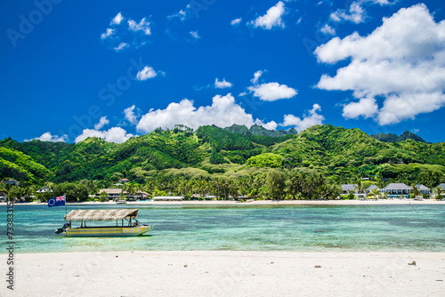 Tropical bay, paradise destination on the Cook Islands. Rarotonga coast with palm tree during a sunny day. One boat on the sea. Blue sky with clouds. Partly cloudy.