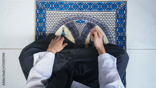 Top view of man muslim with praying hand on the prayer mat while holding prayer beads