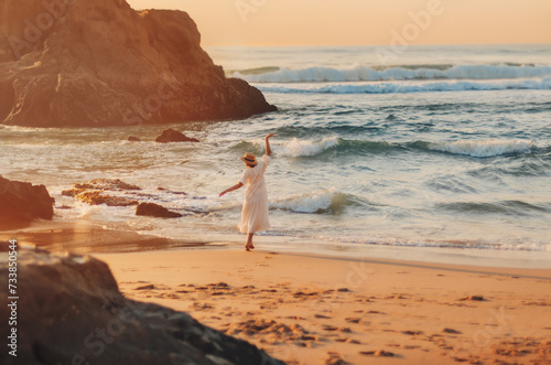 a young girl in a white dress walks on the beautiful ocean shore with sunset light and beautiful sea waves