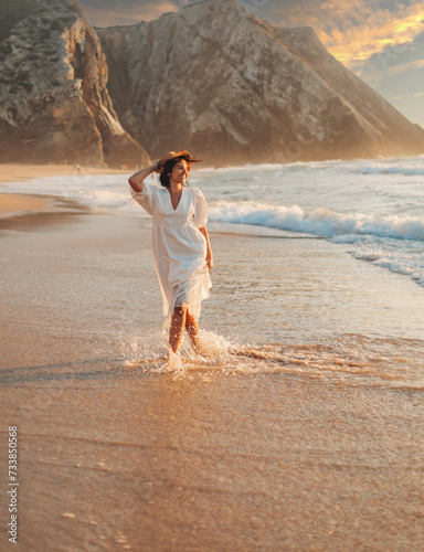 a young girl in a white dress walks on the beautiful ocean shore with sunset light and beautiful sea waves