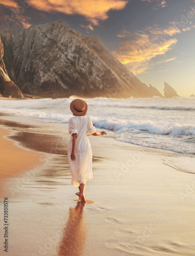 a young girl in a white dress walks on the beautiful ocean shore with sunset light and beautiful sea waves
