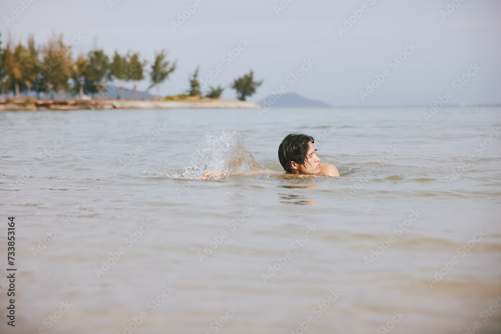 Active Asian Man Enjoying a Tropical Swim in the Refreshing Blue Ocean Water on a Relaxing Vacation Active Asian Man Enjoying a Tropical Swim in the Refreshing Blue Ocean Water on a Relaxing Vacation