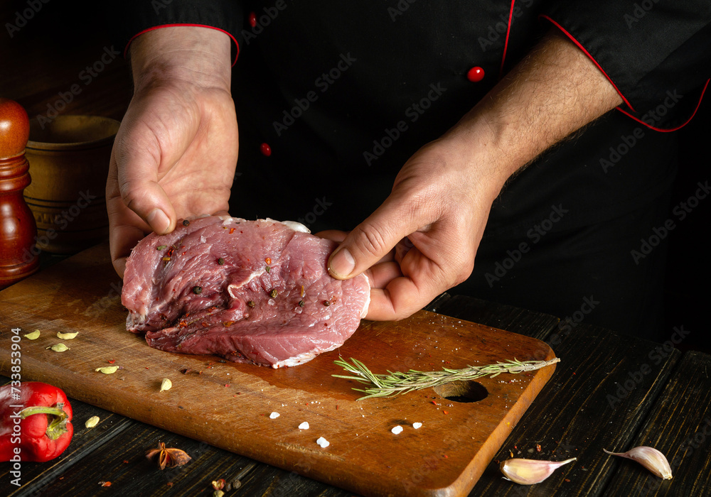 A butcher is preparing a beef steak on the kitchen table for barbecue for lunch. Chef hands with a cut piece of raw veal meat.