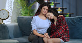 Indian Asian happy lesbian teen age couple sitting sofa couch fun enjoy tender moment indoor home. India gen z lgbt young model female girl lover smiling hold hand spend day time house