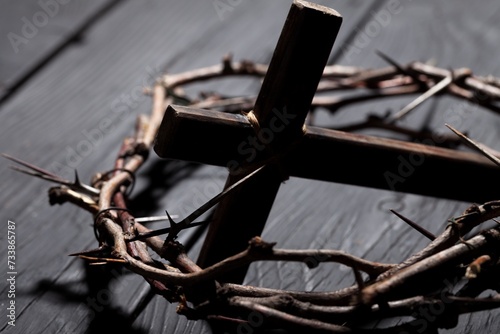 Christian cross with crown thorns on dark desk.