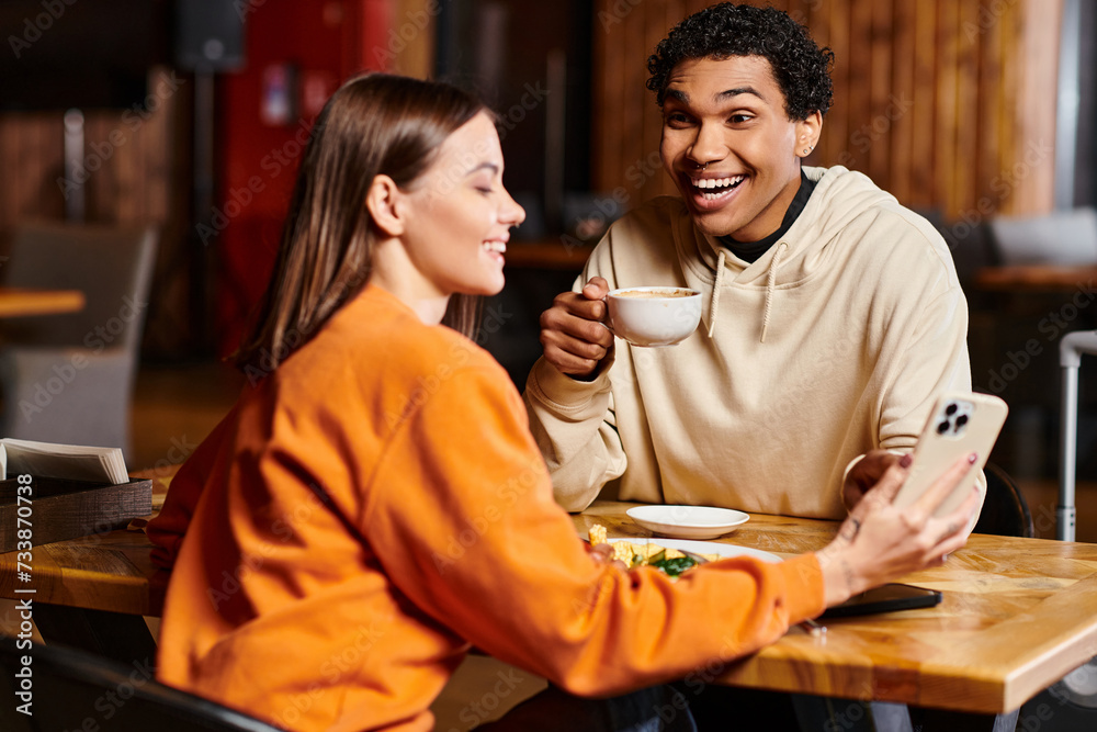 cheerful black man looking at woman sit at a wooden table with smartphone in local cafe, lunch time cheerful black man looking at woman sit at a wooden table with smartphone in local cafe, lunch time
