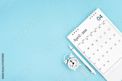 April 2024, Monthly desk calendar for 2024 year and alarm clock with paper clips on blue color background.