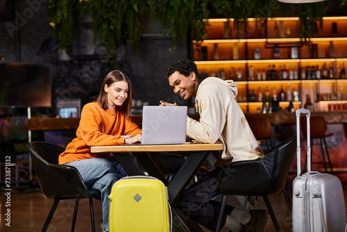 black man and woman looking at laptop on cafe table, with their luggage beside them, travel © LIGHTFIELD STUDIOS