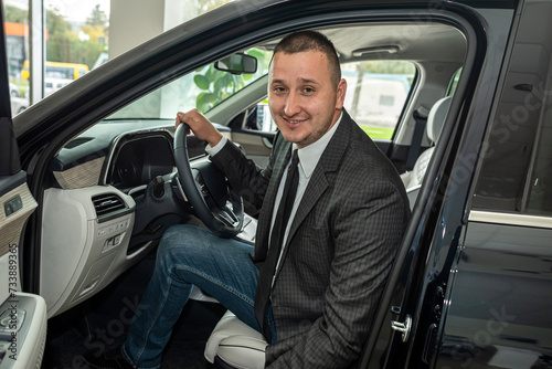 Cheerful man client holding key sitting inside new auto at dealership