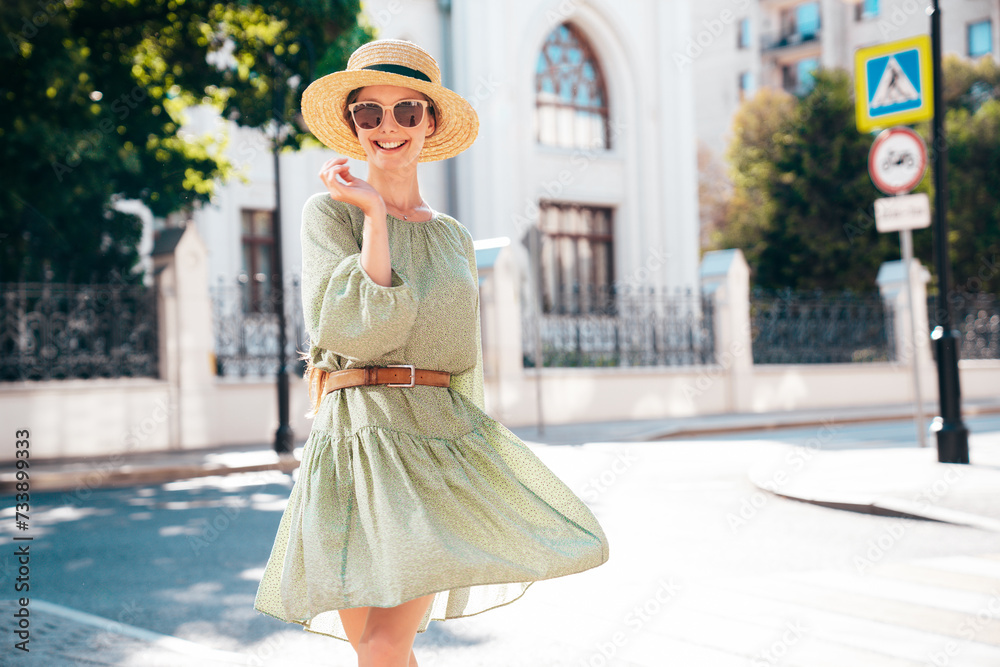 Portrait of young beautiful smiling brunette woman in trendy summer dress. Sexy carefree woman posing in street. Positive model outdoors at sunny day. Cheerful and happy. In hat and sunglasses