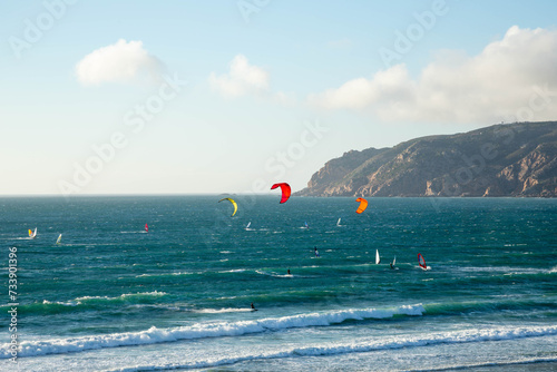 View of the Atlantic Ocean with surfers and windsurfers in the water against of the blue sky and mountains. A beautiful landscape with a view of the ocean. Praia do Guin, Cascais. Portugal. photo