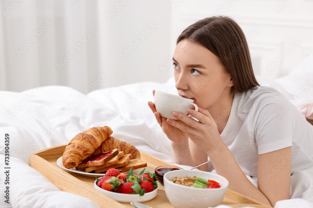 Beautiful woman drinking coffee near tray with breakfast on bed. Space for text Beautiful woman drinking coffee near tray with breakfast on bed. Space for text