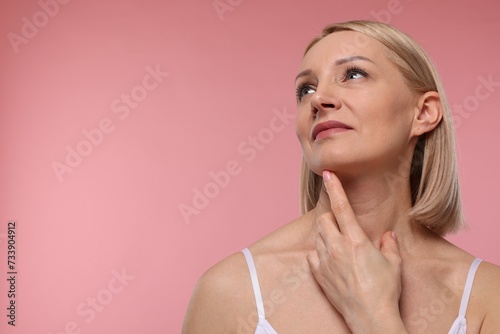 Beautiful woman touching her neck on pink background. Space for text