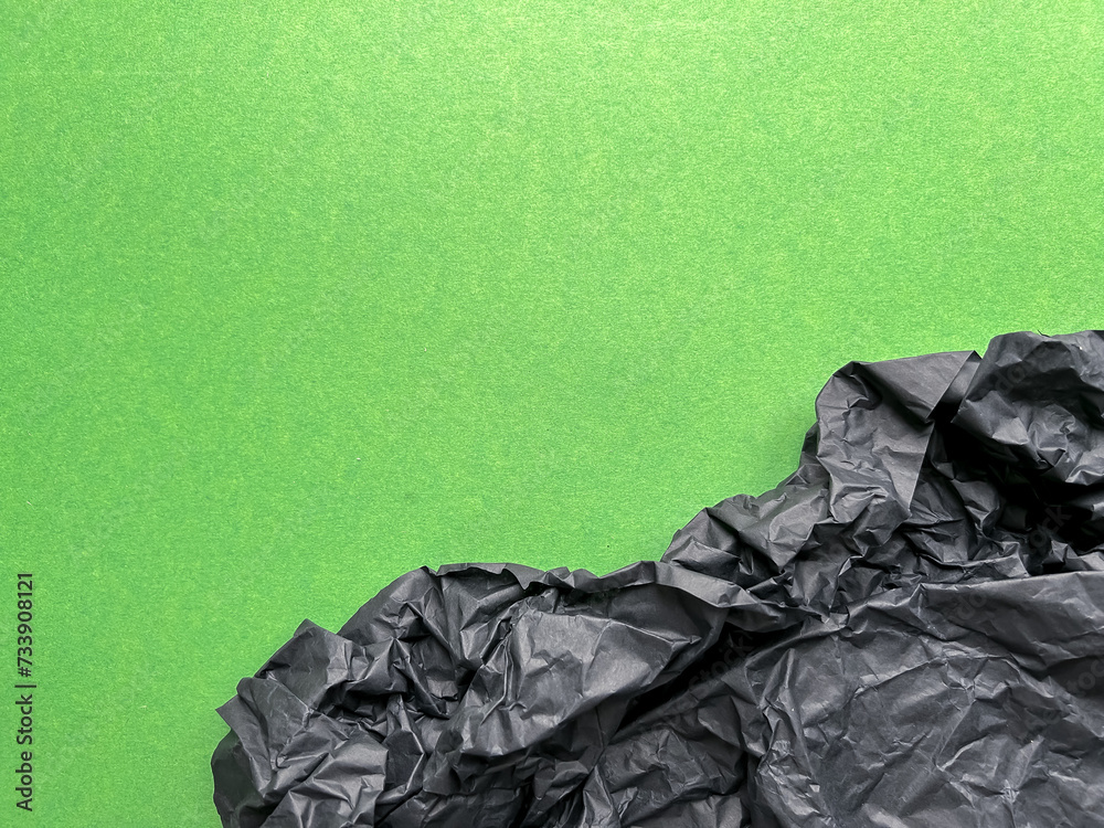 Texture of crumpled black paper on green background, paper background design with space for text, pollution of the planet