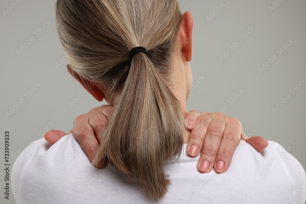 Naklejka premium Mature woman suffering from pain in her neck on grey background, back view
