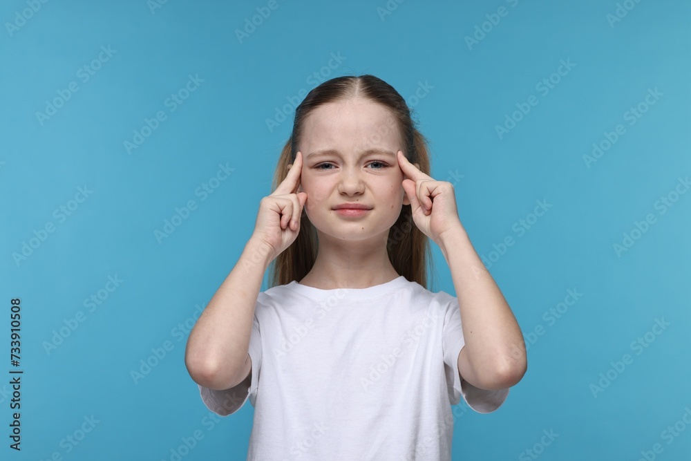 Little girl suffering from headache on light blue background Little girl suffering from headache on light blue background