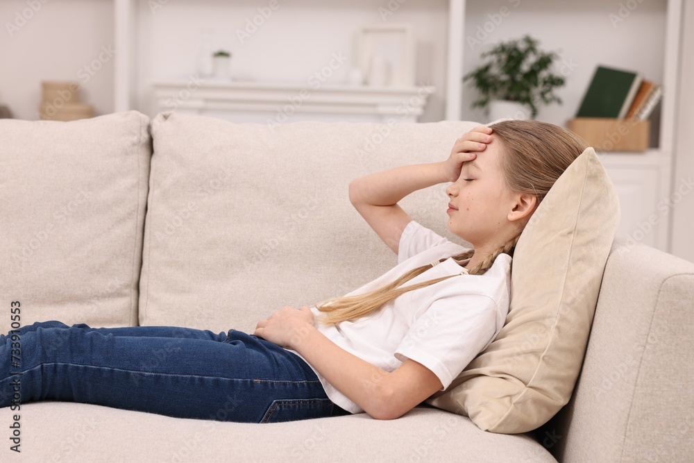 Little girl suffering from headache on sofa indoors Little girl suffering from headache on sofa indoors